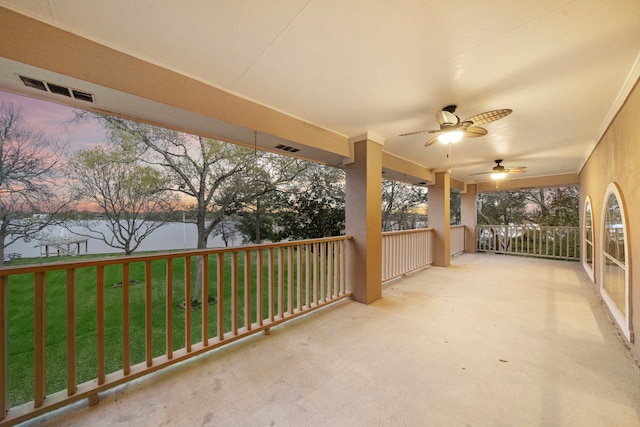 patio terrace at dusk featuring a water view, a lawn, and ceiling fan