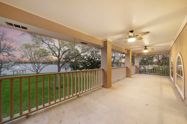 patio terrace at dusk with a lawn, a water view, ceiling fan, and visible vents