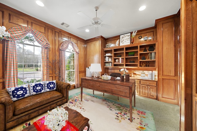 carpeted home office featuring wooden walls and ceiling fan