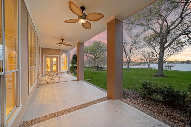 patio terrace at dusk featuring french doors, a water view, a yard, and ceiling fan