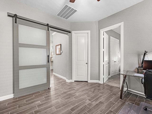 office with a barn door, wood-type flooring, and ceiling fan