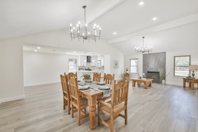 dining space with beam ceiling, a high end fireplace, an inviting chandelier, and light wood-type flooring