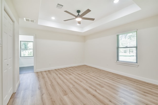 empty room featuring ceiling fan, light wood-type flooring, and a raised ceiling