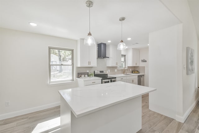 kitchen with wall chimney range hood, appliances with stainless steel finishes, a kitchen island, hanging light fixtures, and white cabinets