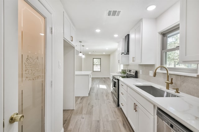 kitchen featuring wall chimney range hood, stainless steel appliances, sink, plenty of natural light, and white cabinets