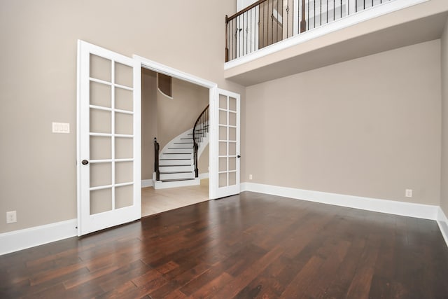 empty room featuring french doors, wood-type flooring, and a towering ceiling