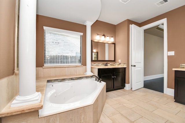 bathroom with vanity, a relaxing tiled tub, and decorative columns