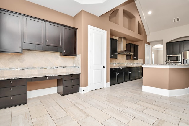 kitchen featuring wall chimney exhaust hood, lofted ceiling, light stone countertops, and built in desk