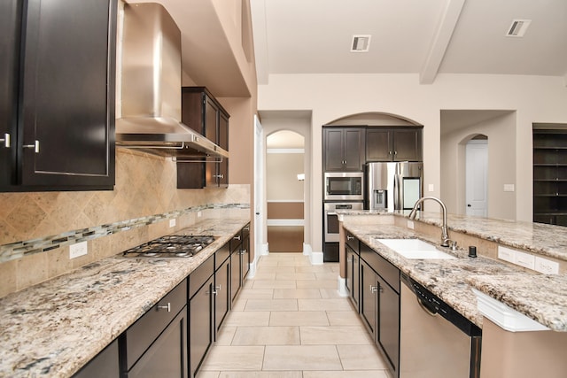 kitchen with tasteful backsplash, wall chimney range hood, sink, stainless steel appliances, and light stone counters