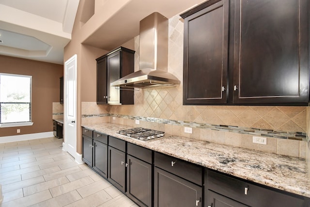 kitchen with backsplash, wall chimney range hood, dark brown cabinets, and stainless steel gas stovetop