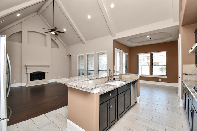 kitchen featuring vaulted ceiling with beams, light hardwood / wood-style flooring, a center island with sink, light stone countertops, and ceiling fan