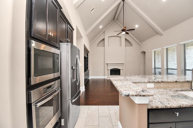 kitchen featuring dark brown cabinetry, light wood-type flooring, appliances with stainless steel finishes, light stone counters, and ceiling fan