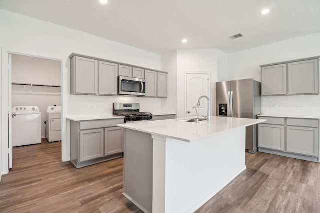 kitchen featuring a center island with sink, sink, independent washer and dryer, appliances with stainless steel finishes, and wood-type flooring