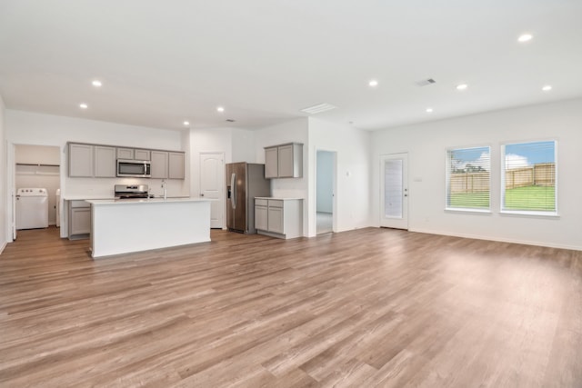 unfurnished living room with light wood-type flooring, sink, and washer / clothes dryer