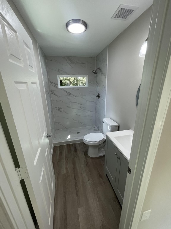 bathroom featuring vanity, hardwood / wood-style floors, a tile shower, and toilet