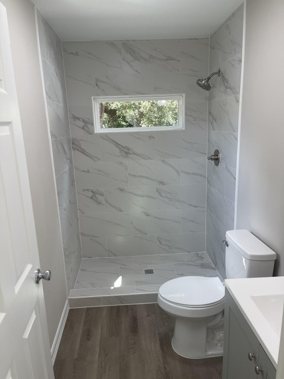 bathroom with vanity, toilet, hardwood / wood-style flooring, and a tile shower