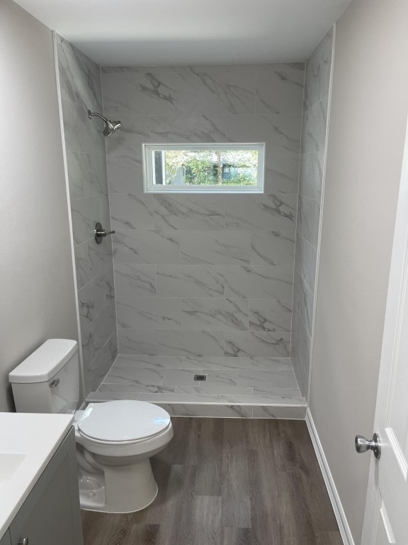 bathroom with vanity, toilet, wood-type flooring, and a tile shower