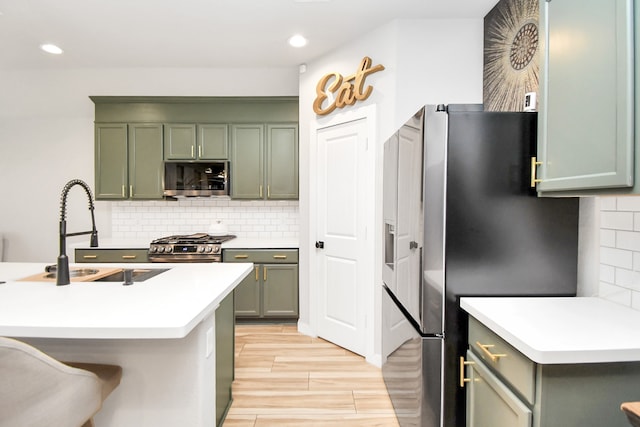 kitchen featuring backsplash, appliances with stainless steel finishes, green cabinets, light wood-type flooring, and sink