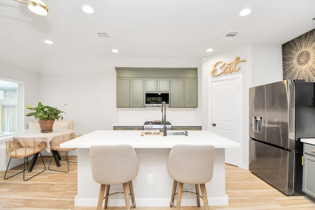 kitchen featuring light hardwood / wood-style floors, stainless steel appliances, a center island with sink, decorative backsplash, and a breakfast bar