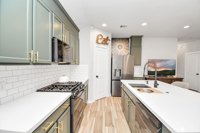 kitchen with stainless steel appliances, green cabinets, sink, a kitchen island with sink, and backsplash