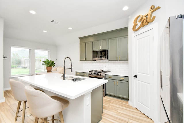 kitchen with stainless steel appliances, sink, a kitchen breakfast bar, light hardwood / wood-style floors, and a kitchen island with sink