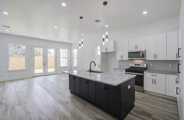 kitchen featuring hanging light fixtures, a center island with sink, sink, white cabinetry, and appliances with stainless steel finishes