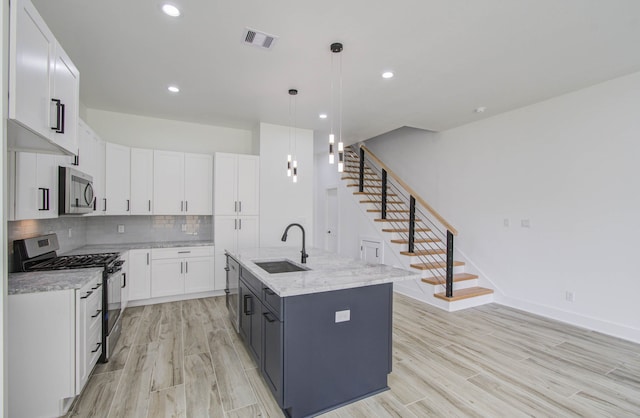 kitchen featuring an island with sink, sink, decorative light fixtures, white cabinetry, and appliances with stainless steel finishes