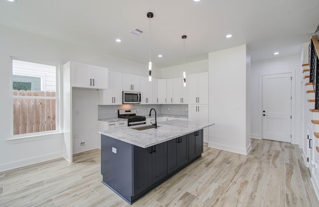 kitchen with appliances with stainless steel finishes, an island with sink, white cabinetry, decorative light fixtures, and light stone counters