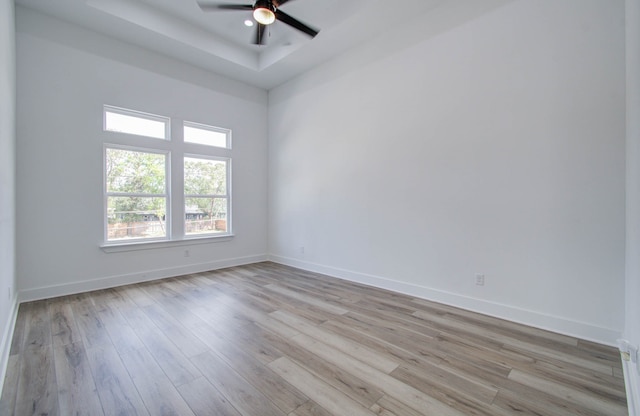 unfurnished room with ceiling fan, light wood-type flooring, and a raised ceiling