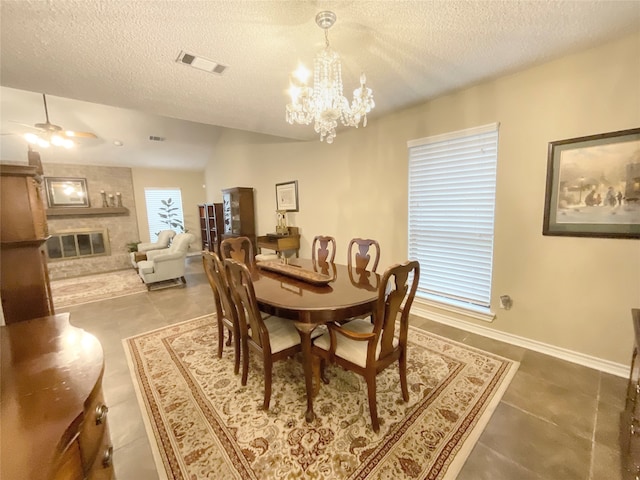 tiled dining room with a textured ceiling, a large fireplace, and ceiling fan with notable chandelier