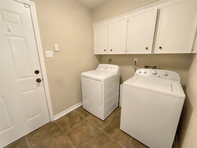 laundry area with dark tile patterned floors, washing machine and clothes dryer, and cabinets