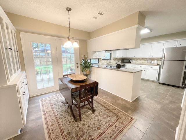 kitchen featuring stainless steel fridge, white cabinets, decorative light fixtures, and tasteful backsplash