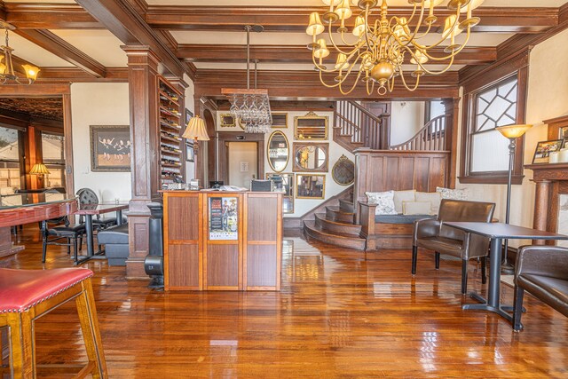 interior space with hardwood / wood-style flooring, decorative columns, ornamental molding, beamed ceiling, and a notable chandelier