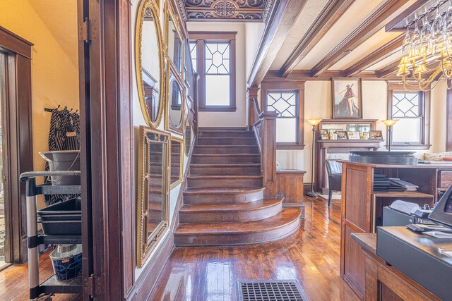 stairway featuring beamed ceiling, ornamental molding, hardwood / wood-style floors, and an inviting chandelier