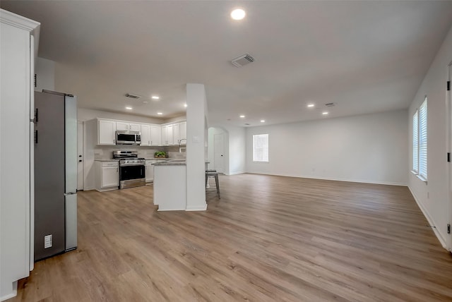 kitchen featuring white cabinets, a breakfast bar, light wood-type flooring, and appliances with stainless steel finishes