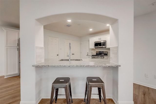 kitchen with light stone countertops, sink, stainless steel appliances, a kitchen breakfast bar, and white cabinets