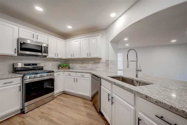 kitchen featuring white cabinets, sink, light wood-type flooring, light stone counters, and stainless steel appliances