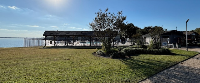 view of dock with a water view, a community pool, fence, and a lawn