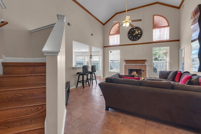 living room with a tile fireplace, ceiling fan, high vaulted ceiling, crown molding, and light tile patterned flooring