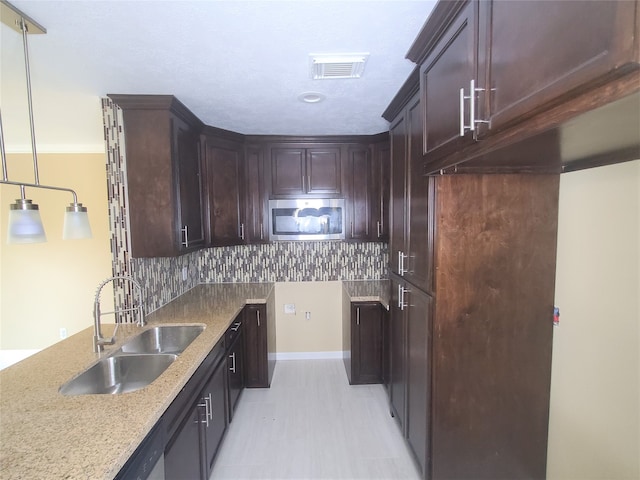 kitchen featuring light stone countertops, sink, dark brown cabinetry, pendant lighting, and decorative backsplash