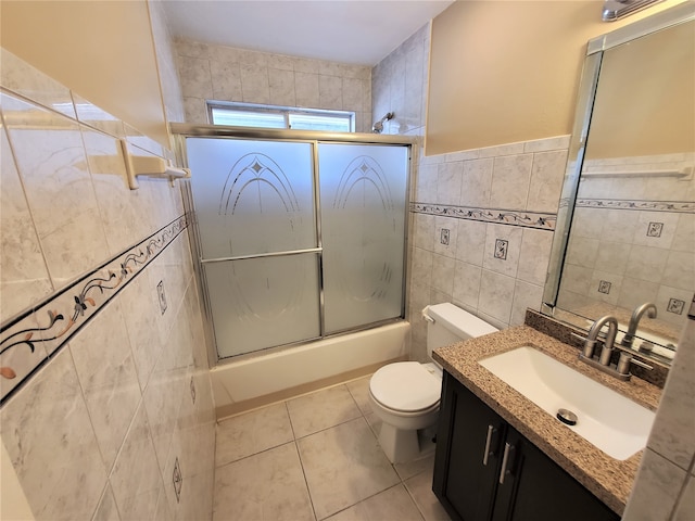 full bathroom with tile patterned floors, toilet, bath / shower combo with glass door, tile walls, and vanity