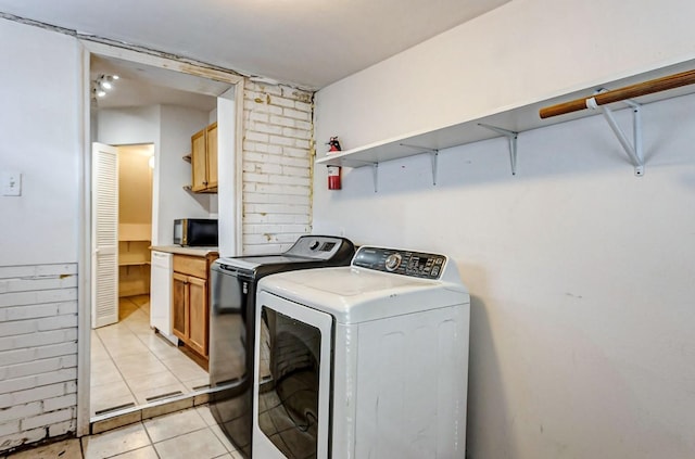 laundry area featuring light tile patterned floors, washing machine and dryer, and brick wall