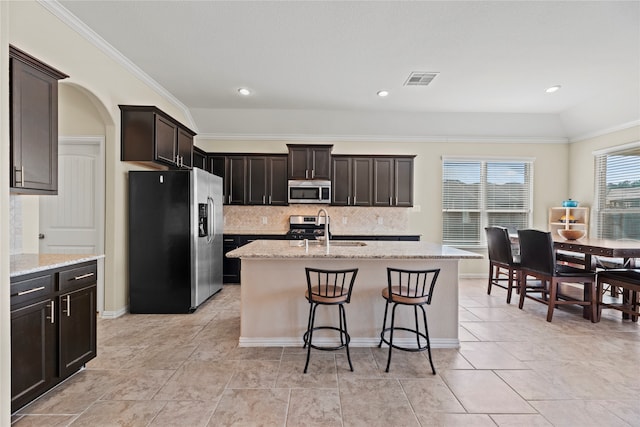 kitchen featuring sink, backsplash, stainless steel appliances, vaulted ceiling, and a kitchen island with sink