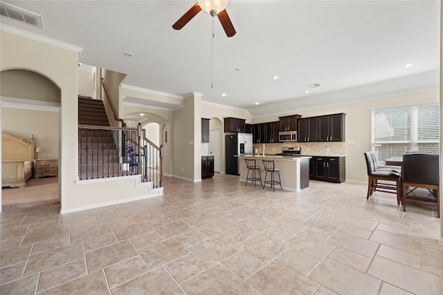 kitchen with ceiling fan, a kitchen breakfast bar, a kitchen island with sink, ornamental molding, and stainless steel appliances