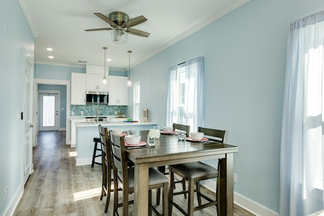 dining area with light hardwood / wood-style floors, ornamental molding, and ceiling fan