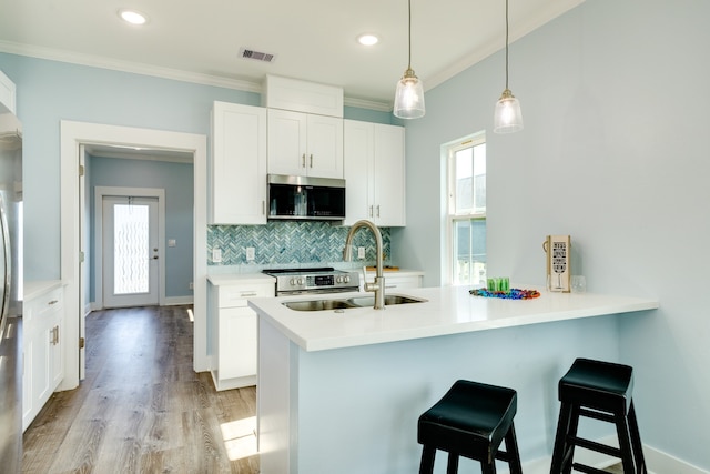 kitchen featuring white cabinets, appliances with stainless steel finishes, light hardwood / wood-style flooring, crown molding, and decorative light fixtures