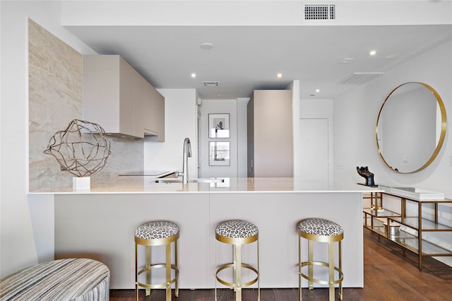 kitchen featuring decorative backsplash, dark hardwood / wood-style floors, kitchen peninsula, sink, and a kitchen bar