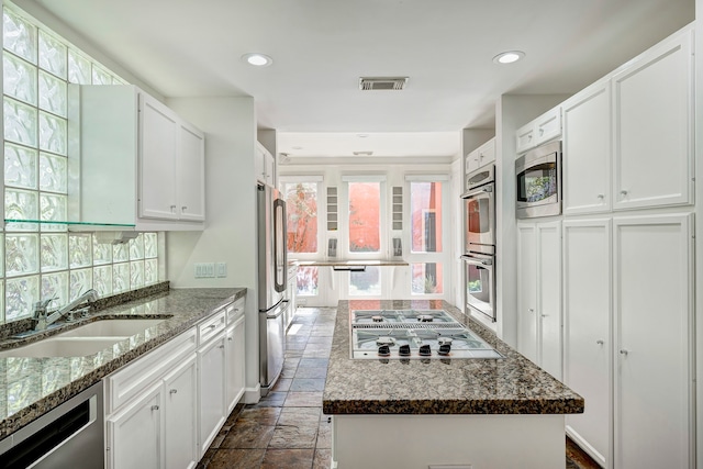 kitchen featuring appliances with stainless steel finishes, sink, a center island, dark stone counters, and white cabinets