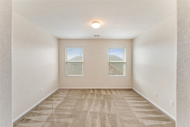 carpeted empty room with visible vents, baseboards, and a textured wall