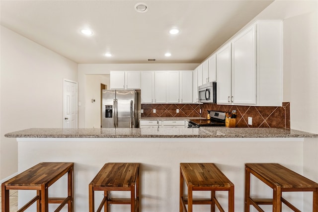 kitchen with backsplash, appliances with stainless steel finishes, a peninsula, and white cabinetry